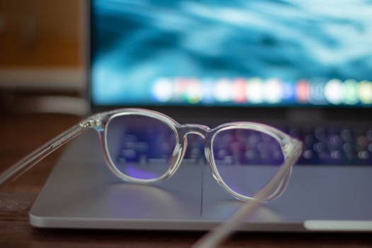 A close-up of a blue light reflecting glasses beside a laptop